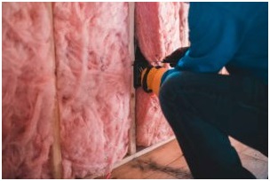 Contractor installing pink fiberglass batt insulation in a wall.